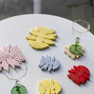 Klevering Blume leaf-shaped coasters in red, blue, yellow and beige, close up on a white surface