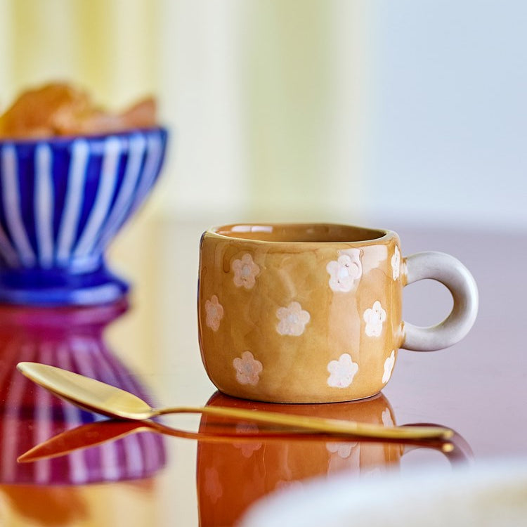 Bloomingville Nini mustard floral cup on a table with a blue glass