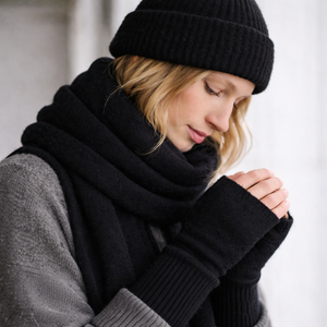 Woman wearing fingerless knit mittens, beanie and scarf in black